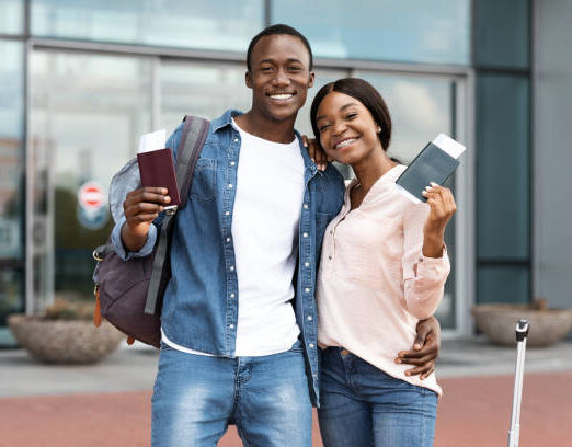 Ready For Vacasion. Excited Black Spouses Posing Near Airport With Passports In Hands, Smiling At Camera, Free Space